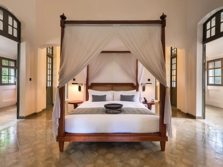 Bright, airy bedroom with a neatly made canopy bed and white curtains