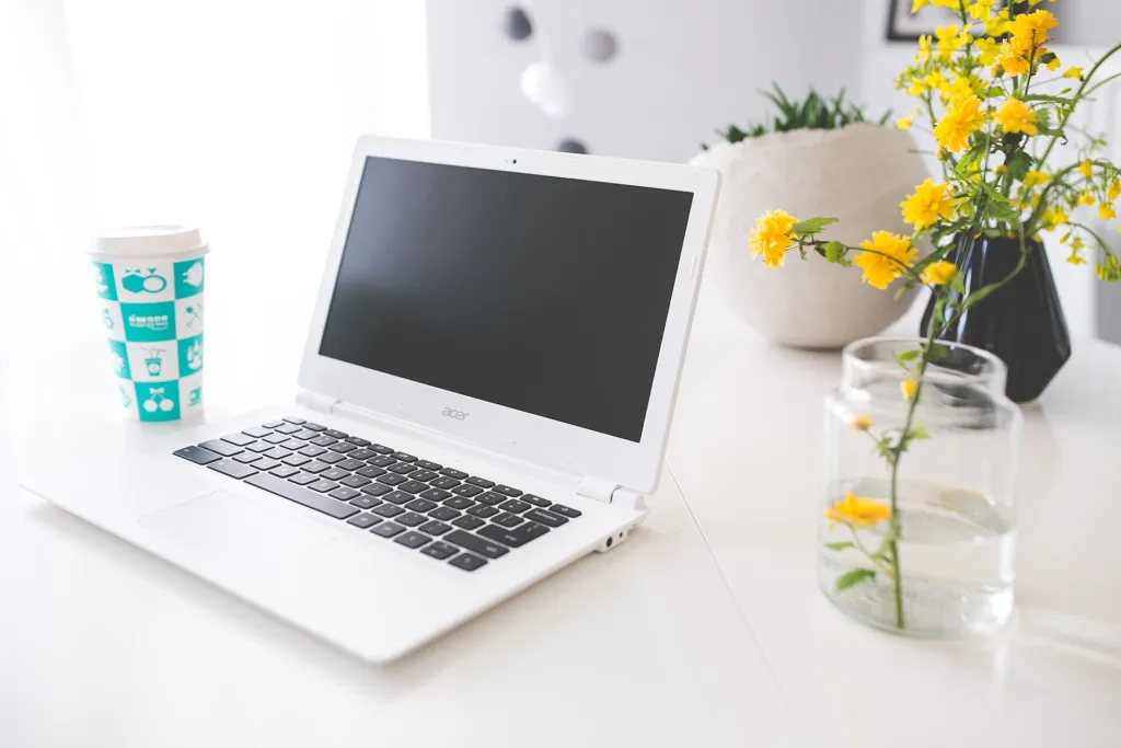 White laptop on a bright desk beside a vase of yellow flowers and a coffee cup
