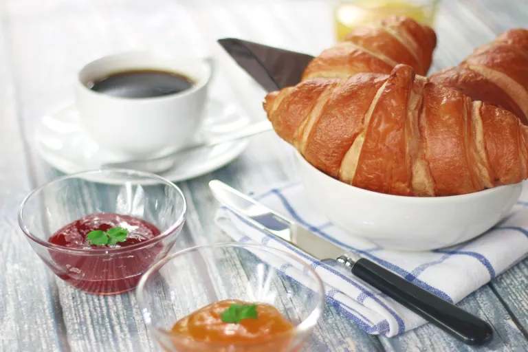 Cup of black coffee with a croissant and jam on a breakfast table