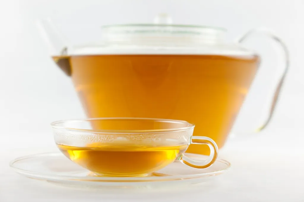 Glass teapot and cup of golden herbal tea on a saucer