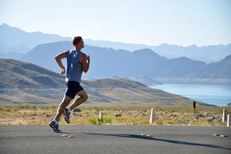 Runner jogging along a sunny road with mountains and a lake in the background