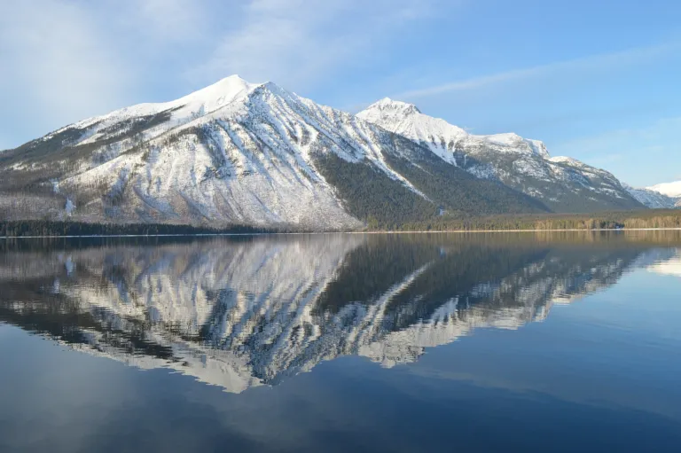 Snow-capped mountain reflected in a calm, still lake under a blue sky