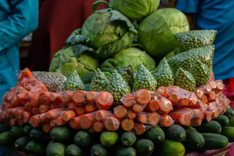 Fresh cabbages, cucumbers and carrots stacked at a market stall