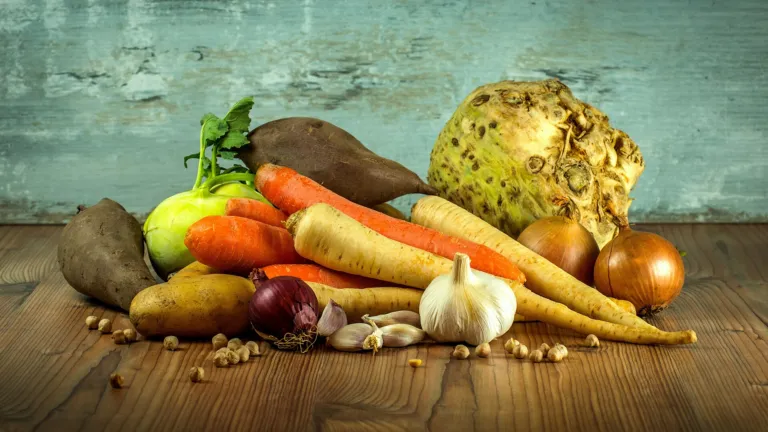 Carrots, parsnips, potatoes, onions, garlic and celeriac arranged on a rustic wooden table