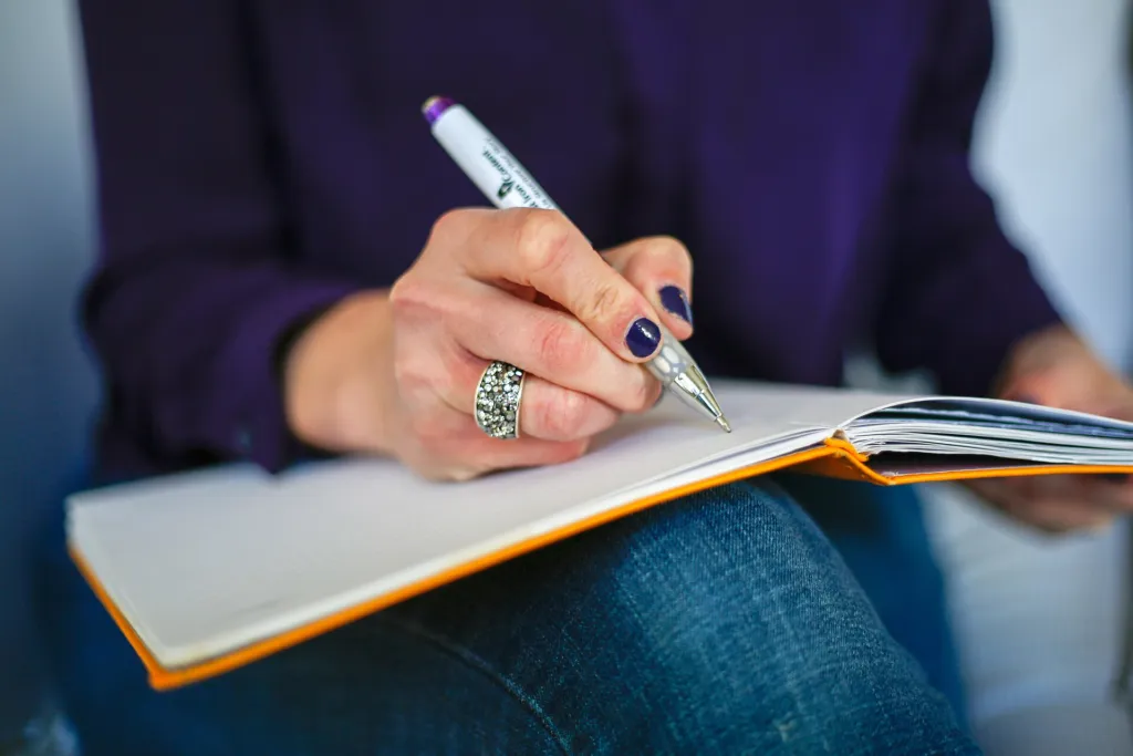 Person writing in an open notebook journal with a pen