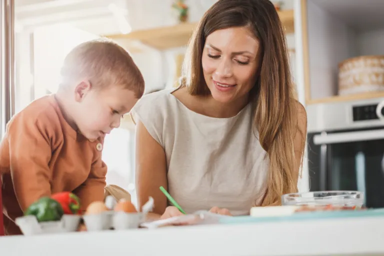 Woman helping a young boy with writing practice at a table
