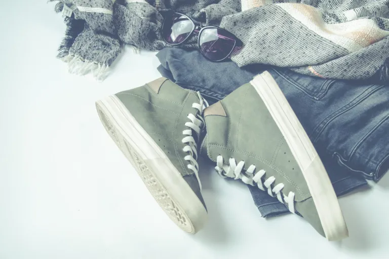 Pair of green canvas sneakers next to folded jeans and a scarf