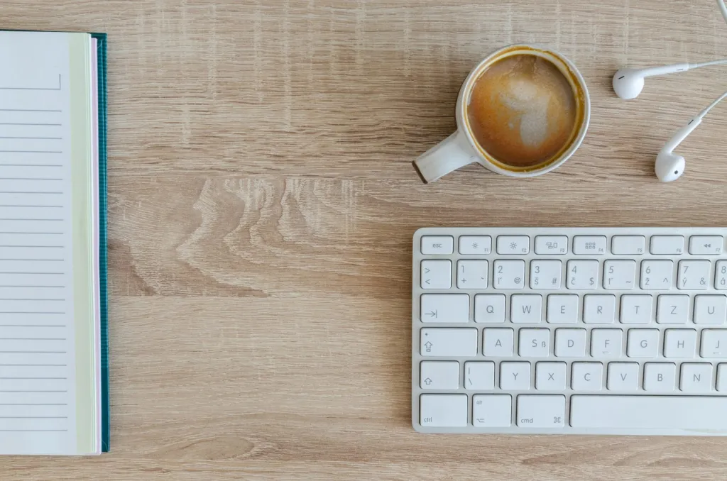 Cup of coffee, notebook and keyboard on a wooden desk seen from above