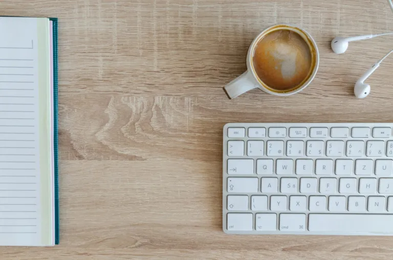 Cup of coffee, notebook and keyboard on a wooden desk seen from above