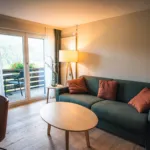 Cozy living room with a green sofa, orange cushions and warm lamp light