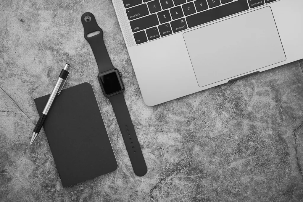Laptop, black notebook, pen and smartwatch on a grey desk