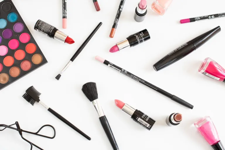 Lipsticks, eyeshadow palette, mascara and makeup brushes on a white surface