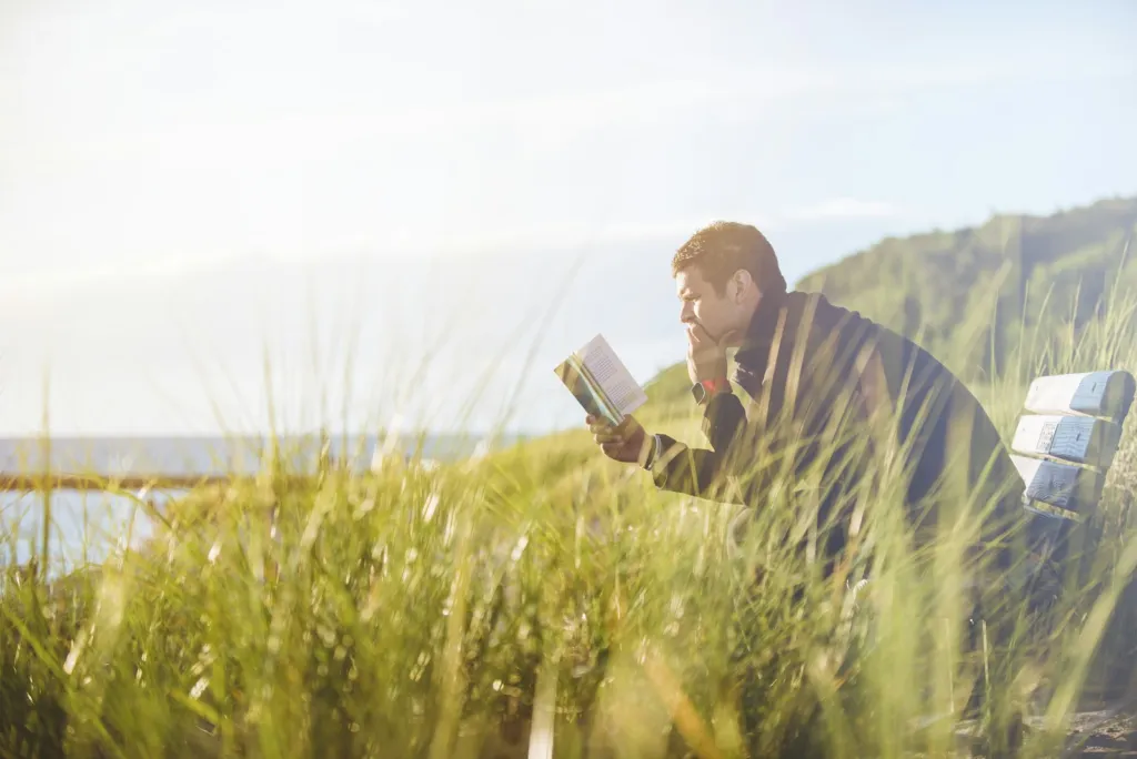 Person reading a book on a quiet lakeside beach on a summer day
