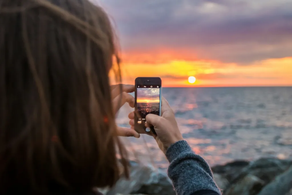 Woman taking a photo of the sunset with her smartphone
