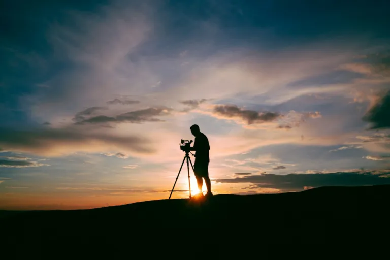 Photographer standing beside a camera on a tripod at sunset