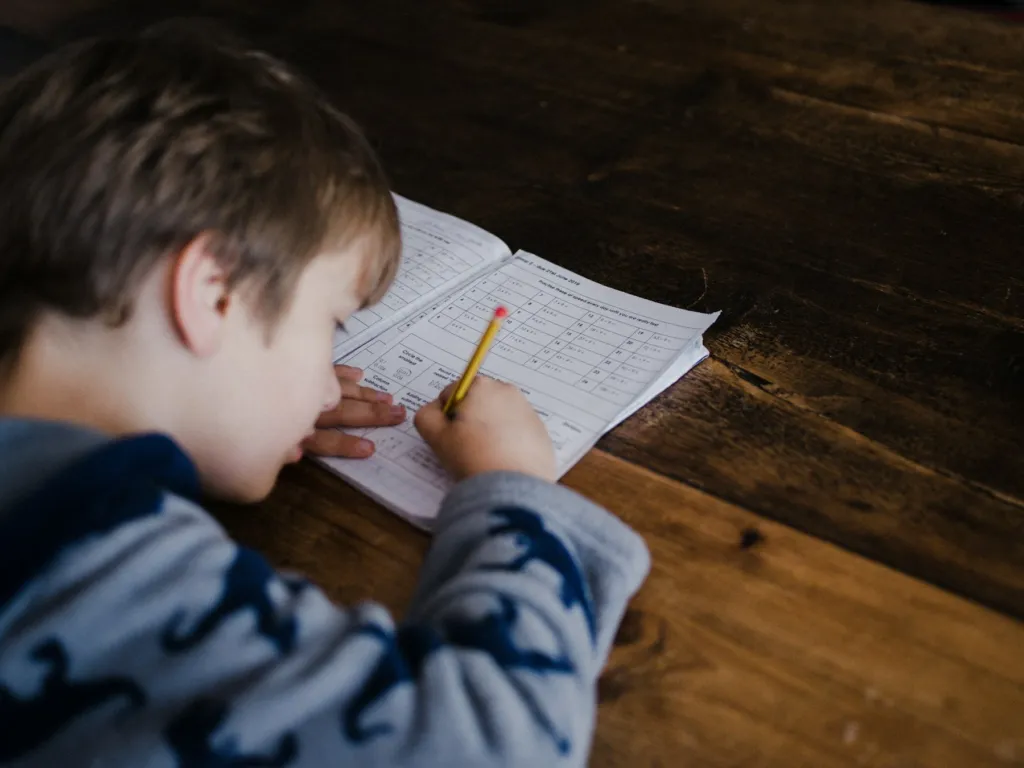 Young student solving math problems with a pencil on a worksheet at a wooden table