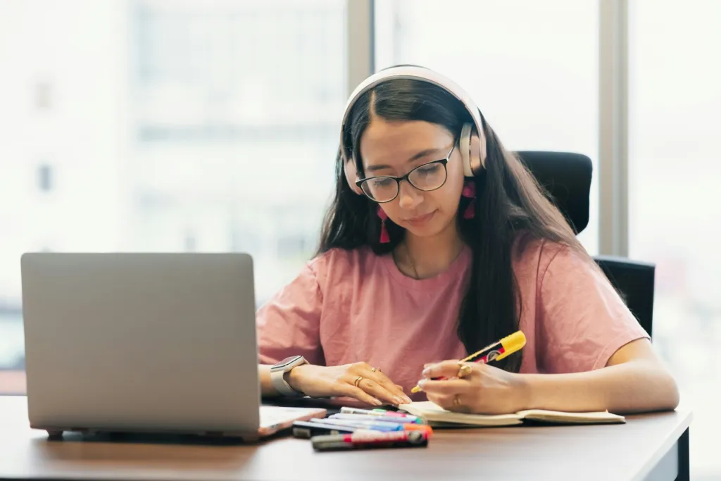 Student with headphones taking notes during an online math tutoring lesson on her laptop