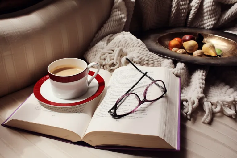 Open book, coffee cup and eyeglasses on a cozy couch
