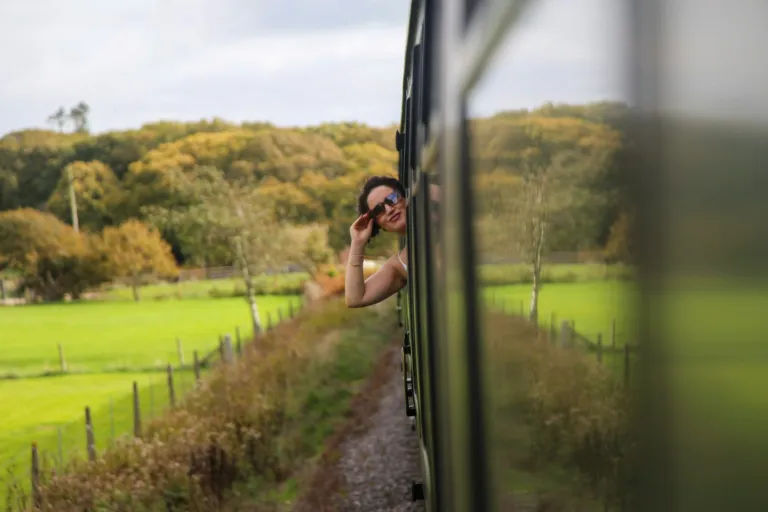 Traveller leaning out of a train window past green fields and trees