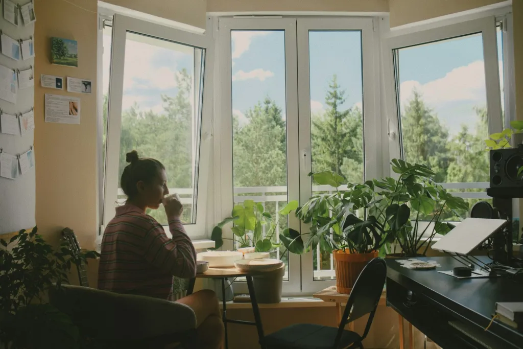 Woman drinking from a mug at a table by a sunlit window in the morning