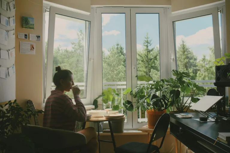 Woman drinking from a mug at a table by a sunlit window in the morning