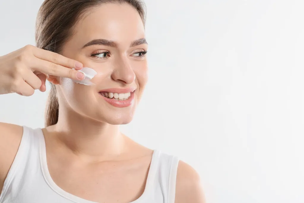 Smiling woman applying moisturising cream to her cheek