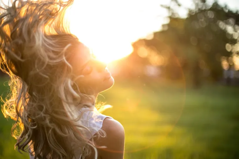 Woman with long, wavy hair backlit by warm sunlight outdoors