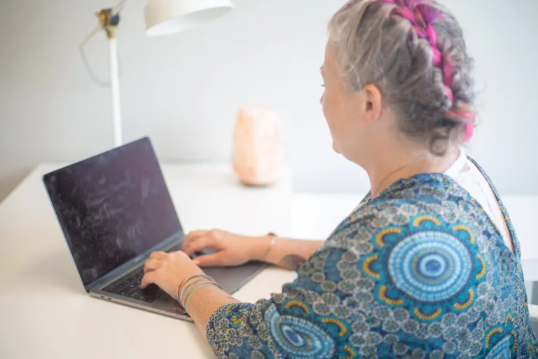 Woman typing on a laptop at a white desk in a bright home office